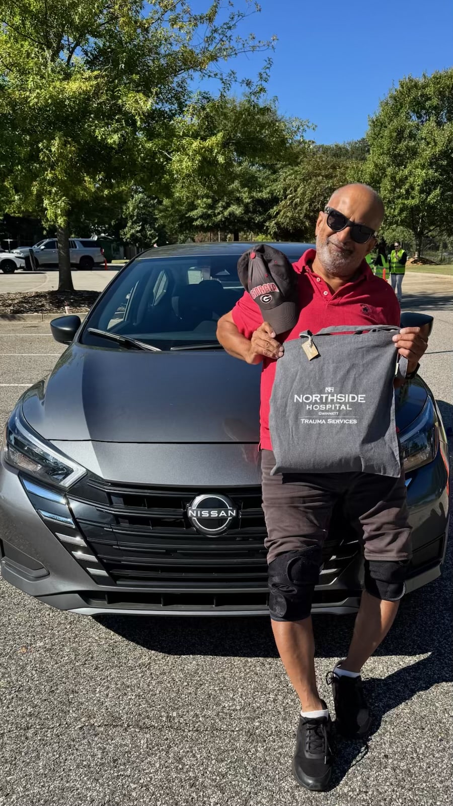 A senior driver holding a take-home bag stands beside his car in the Lawrenceville Senior Center parking lot.